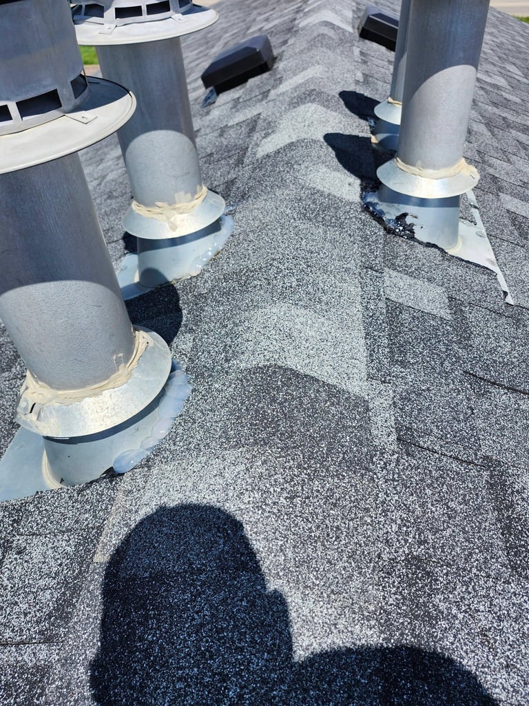 Rooftop showing gray granular surface with white cylindrical HVAC pipes and metal flashing, persons shadow visible in foreground