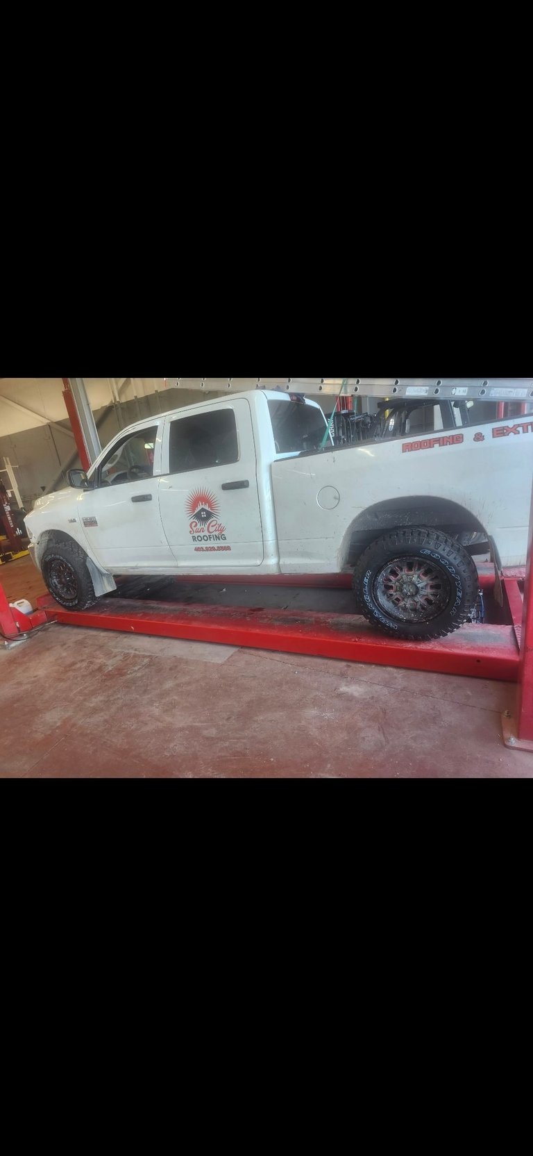 White pickup truck lifted on red service ramp in garage with company logo on door